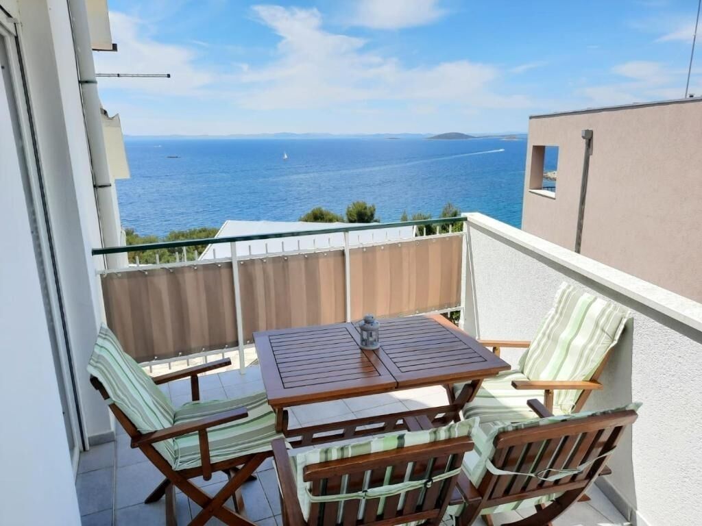 Ein Balkon mit Holztisch und zwei Stühlen, mit Blick auf das Meer.