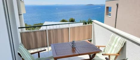 A balcony with a wooden table and two chairs, overlooking a sea view.