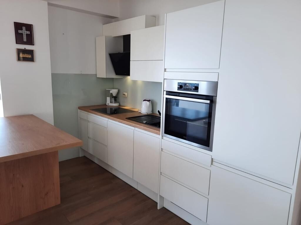 Une cuisine moderne avec des meubles blancs, un plan de travail en bois, un four encastré et une machine à café.