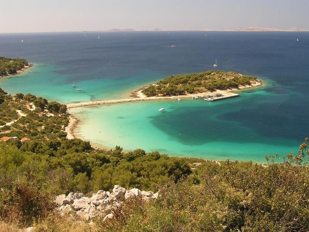 Paesaggio costiero con vista aperta sul mare, una piccola isola e un litorale roccioso.