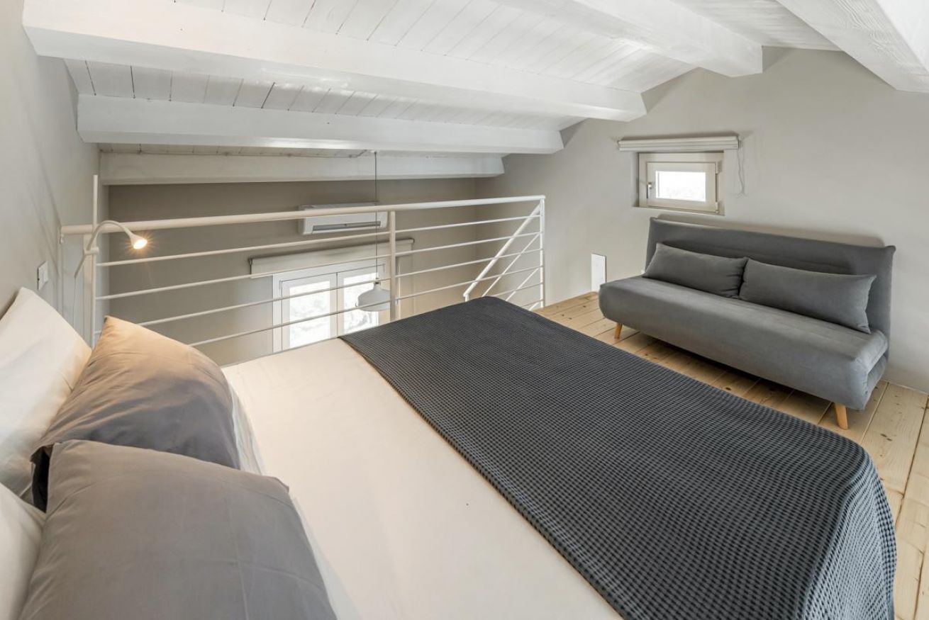 Une chambre à coucher avec un lit, un canapé gris, une fenêtre et un escalier.