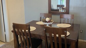 Uma sala de jantar com uma mesa de madeira, quatro cadeiras, um lustre e um espelho na parede.