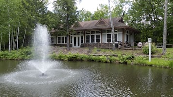 Situated by a serene pond, this lodge features a traditional gabled roof and a covered porch surrounded by lush greenery.