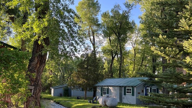 A rustic cabin with a small stream running through a grassy area.