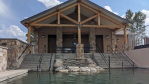 A lodge with a stone facade, wooden beams, and a pool area with steps leading to the entrance.