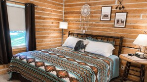 Quarto de cabana de madeira com uma cama, uma mesa de cabeceira, um sonho apanhado e quadros nas paredes.