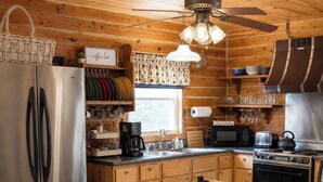 Uma cozinha estilo cabana de madeira com geladeira de aço inoxidável, fogão, micro-ondas e um espaço para café.
