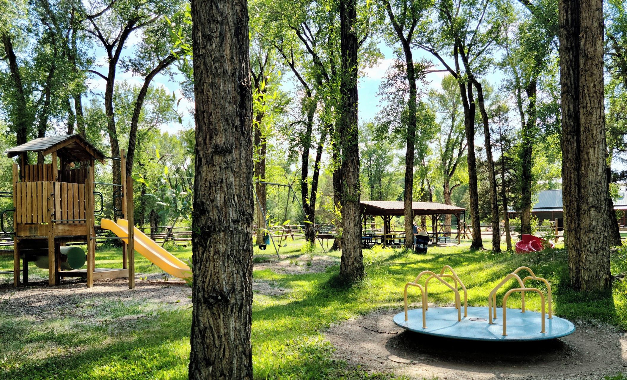 Un parque con un parque infantil de madera, un tobogán, mesas de picnic y un carrusel.