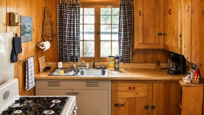 Een keuken in blokhutstijl met houten wanden, een fornuis, een spoelbak en een plafondventilator.