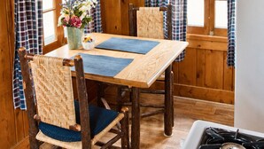 Een houten interieur met een eettafel, stoelen, een fornuis en geruite gordijnen.