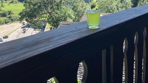 A wooden deck with a glass of beverage, overlooking a mountainous landscape with green fields and trees. - Luxury chalet with panoramic views in the Lötschental, with private carport  (Kippel)