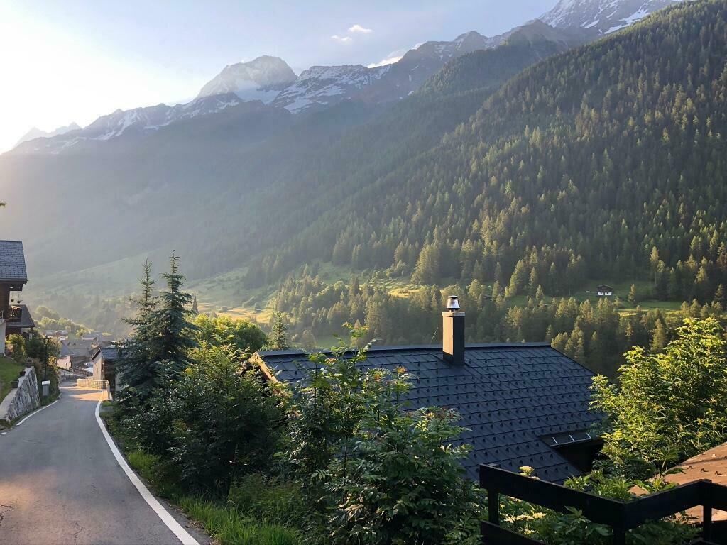 A mountain village with a road leading through it, surrounded by forested hills and mountains.