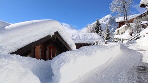 A snow-covered path leading to a wooden building with a sloped roof, surrounded by snow-laden trees and mountains in the background. - Luxury chalet with panoramic views in the Lötschental, with private carport  (Kippel)