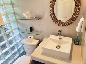Un bany amb vàter, una petita estant de vidre amb productes de tocador, un lavabo i un mirall amb marc de petxina.