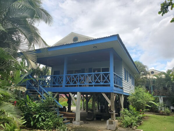 Un edifici blau amb un balcó, envoltat de vegetació abundant.