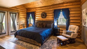 A log cabin bedroom with a large bed, a chair, and a small table. - Montana Wildflower Lodge~sleeps 10 (Red Lodge)
