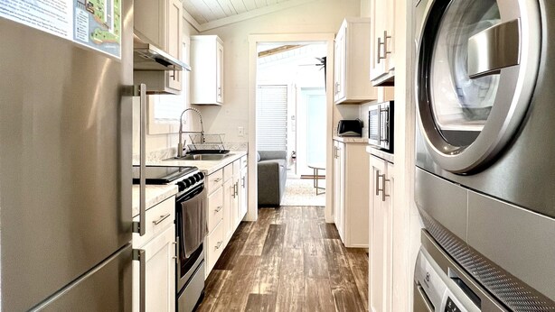 A modern kitchen with stainless steel appliances, wooden flooring, and a view to the living area.