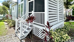 A single-story house with a porch, a small deck, and a front yard with gravel and plants.