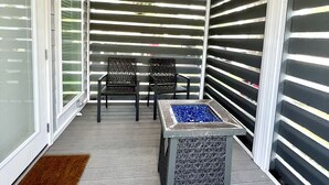 A covered patio with a ceiling fan, two chairs, a fire pit, and a patterned table.