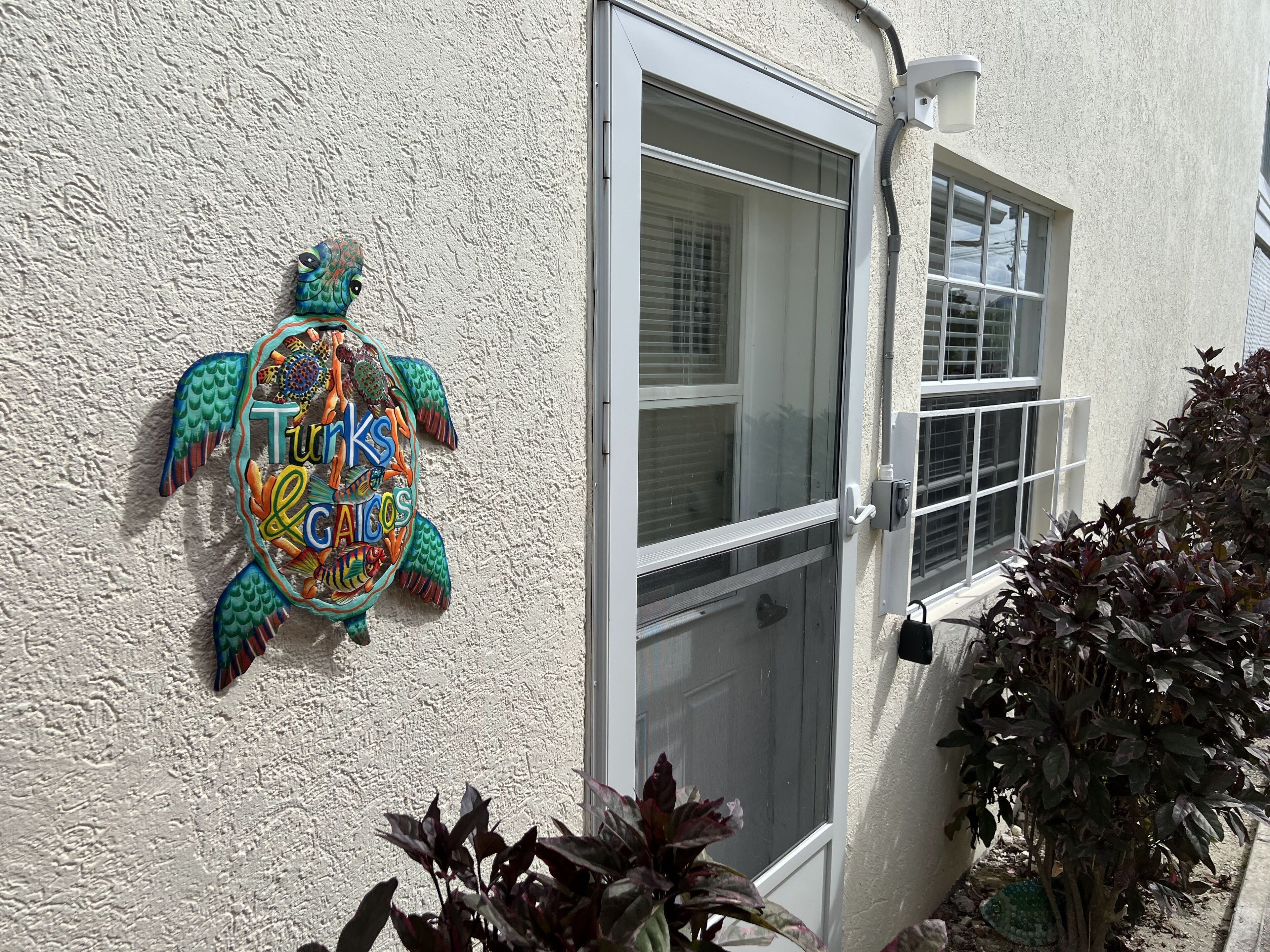 Una casa con una decoración de tortuga colorida en la pared, una puerta corrediza de vidrio y una ventana con persianas.