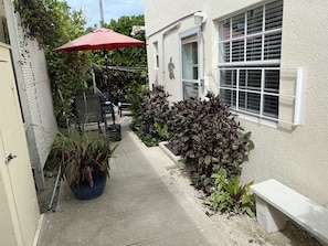 Un petit patio extérieur, avec un parasol rouge, des plantes en pot et un banc.