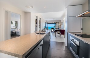 A modern kitchen with a large island, built-in appliances, and a view to the sea.