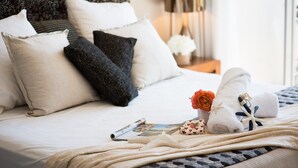 Cama bem arrumada com almofadas, uma toalha enrolada e um pequeno arranjo de flores.