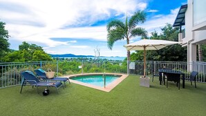 Um quintal com piscina, cadeiras de descanso e mesa com guarda-sóis.