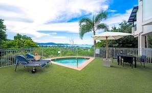 A backyard with a swimming pool, lounge chairs, and a table with umbrellas. - Rendez-vous Chez Leah (Airlie Beach)