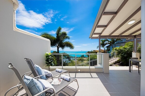 A balcony with a view of the sea, a chair with a towel, and a staircase leading to an upper level.