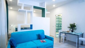 A bright living room with a blue sofa, a glass table, and a striped door. - RED LION APARTMENT x6 (Sorrento)