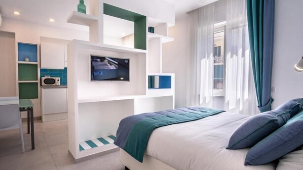 A modern hotel room with a bed, a TV, a desk, and a kitchenette. - RED LION APARTMENT x6 (Sorrento)