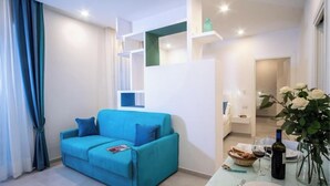 A modern living room with a blue sofa, a dining table with a vase of flowers, and a kitchen area in the background. - RED LION APARTMENT x6 (Sorrento)