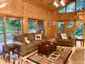 A wooden interior with a sofa, armchair, coffee table, and a rug with animal prints. - “Hollywood Nights” (Old Forge)