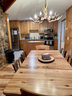 A spacious kitchen with wooden cabinets, a large dining table, and a unique antler chandelier. - “Hollywood Nights” (Old Forge)