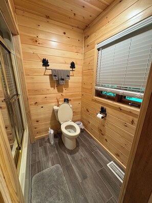 A wooden-paneled bathroom with a toilet, towel rack, and window.