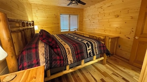 Una habitación de cabaña de madera con una cama, un ventilador de techo y una ventana con persianas.