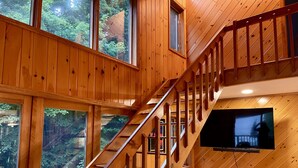 Un interior de madera con una escalera, ventanas amplias y un televisor montado.