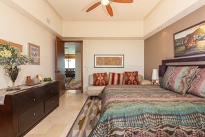 A bedroom with a bed, dresser, ceiling fan, artwork, and a view of the hallway.