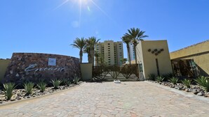 A hotel entrance with a stone pathway, palm trees, and a clear blue sky. - Encanto Living 1104 by Kivoya (Puerto Peñasco)