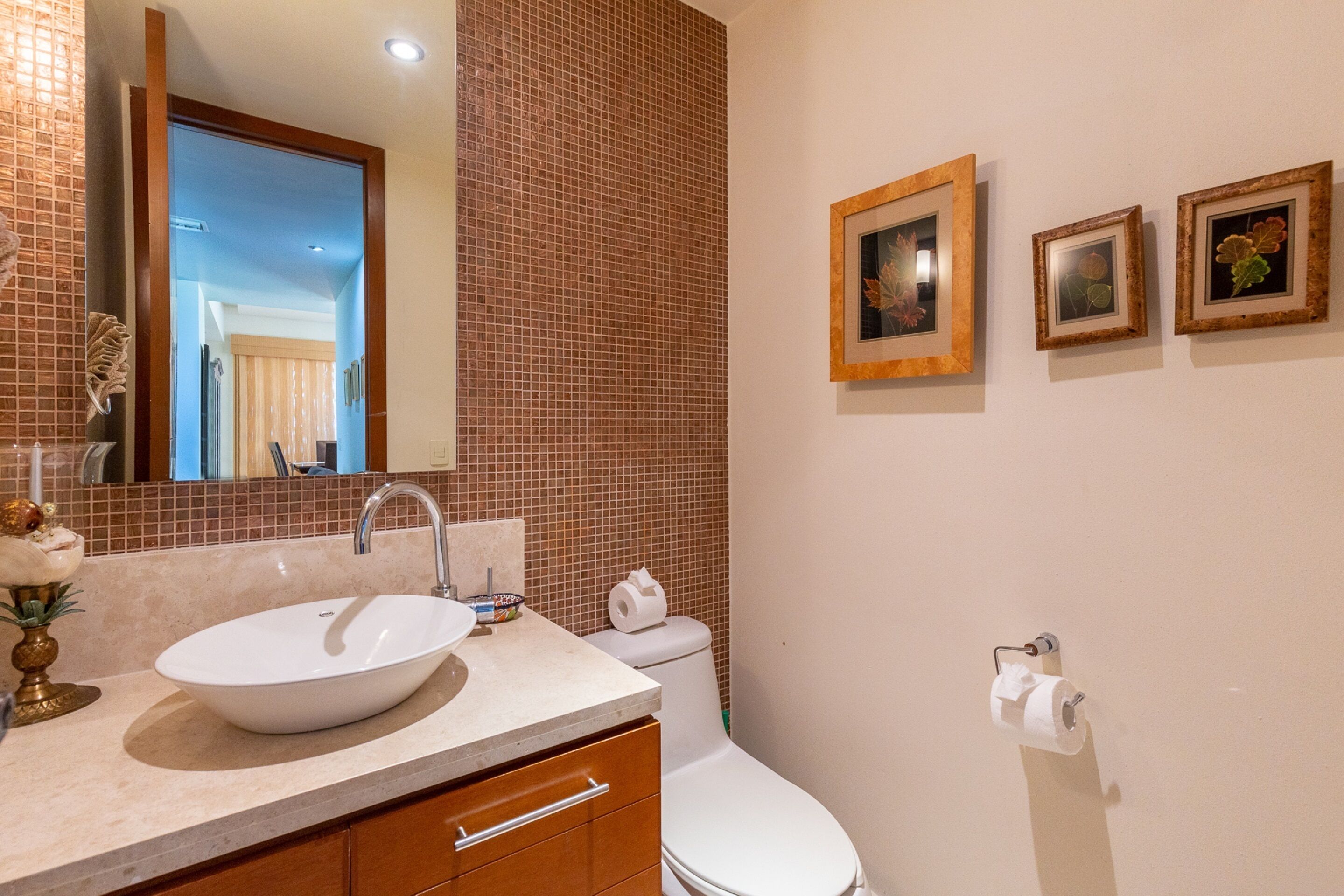 A bathroom with a white sink, a mirror, a toilet, and three framed pictures on the wall.
