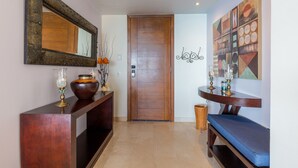 A hallway with a wooden door, a console table with decorative items, a bench, and a wall with abstract art. - Encanto Living 1104 by Kivoya (Puerto Peñasco)