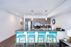 Una cucina moderna con elettrodomestici in acciaio inossidabile, un'isola centrale con sgabelli da bar e illuminazione a sospensione.