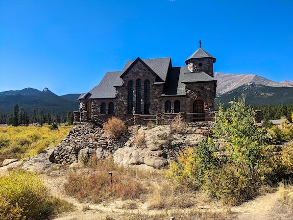 A stone church with a bell tower, set against a mountainous backdrop.