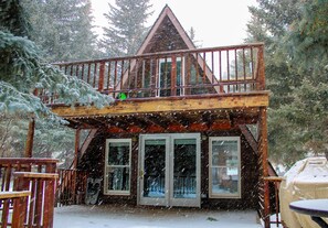 A wooden cabin with a balcony, large windows, and a covered outdoor seating area.