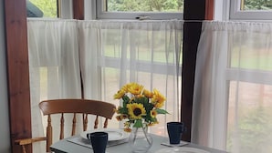 A dining area with a table set for two, a vase with sunflowers, and a view of greenery outside.