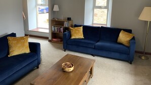 A living room with two blue sofas, a wooden coffee table, a bookshelf, and a lamp.