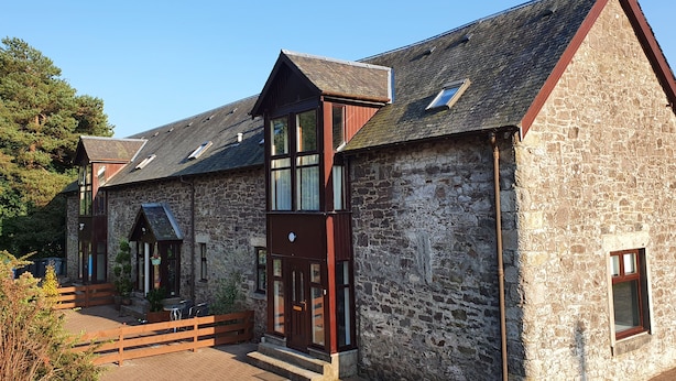 A stone building with a wooden facade, large windows, and a sloped roof.
