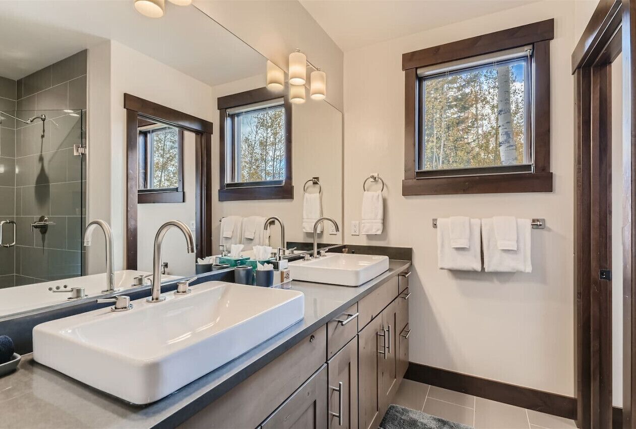 A modern bathroom with two sinks, a large mirror, and a shower area.