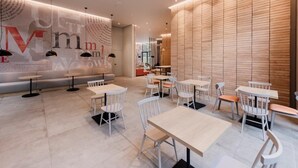 Ein modernes Café mit runden Tischen und weißen Stühlen, eine Holzwand mit vertikalen Lamellen und eine Sitzecke mit einer Bank.